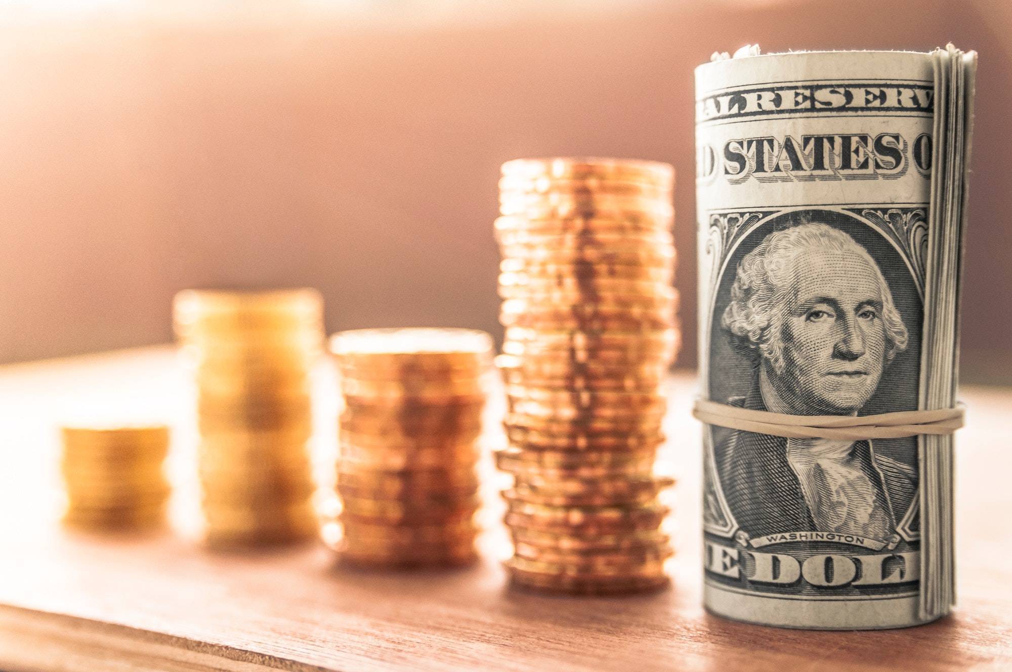 Rolled up US dollar bill with columns of coins in background